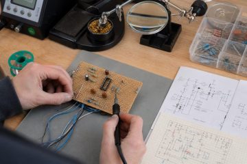 Technician wiring components on a universal prototype PCB from a schematic and grid map