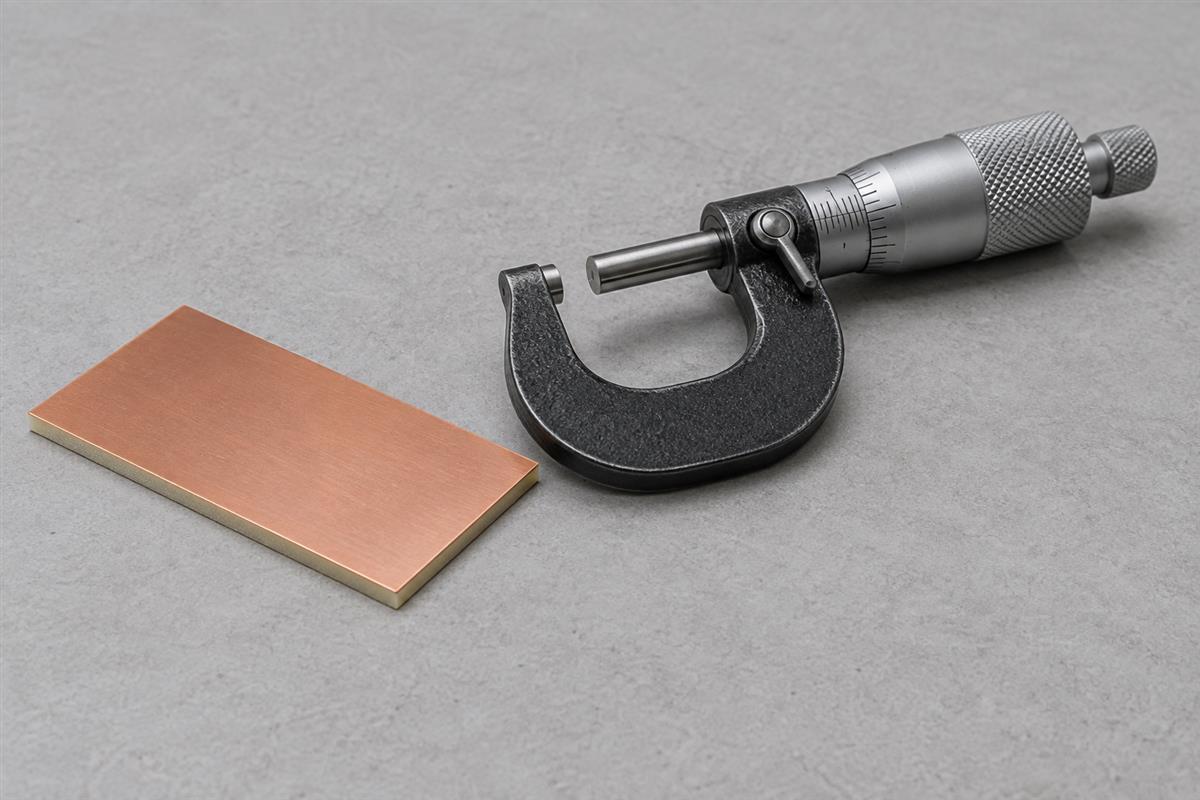 Copper clad laminate coupon beside an outside micrometer, AI illustration