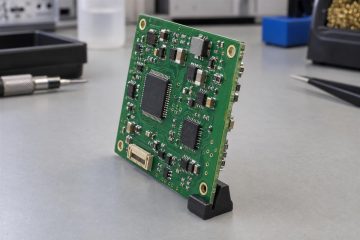 Illustrative populated PCB held at an angle with components visible on both faces