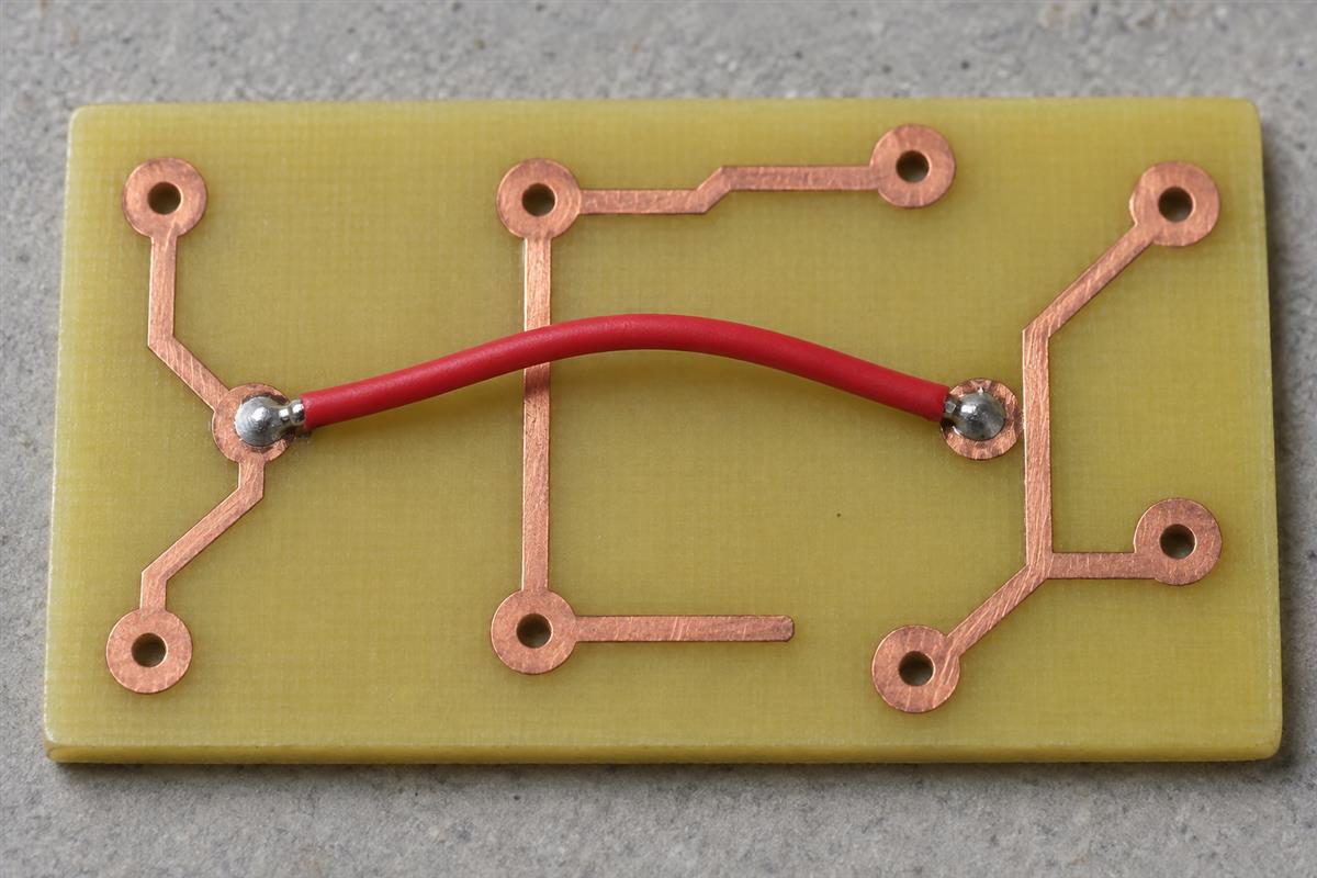 Insulated red wire link crossing a separate copper trace on a teaching coupon, AI illustration